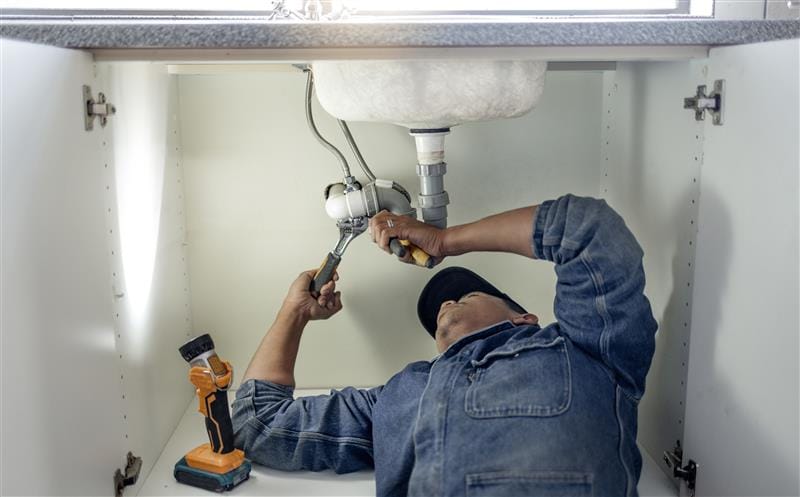 Plumber repairing pipes beneath a bathroom sink in Camas