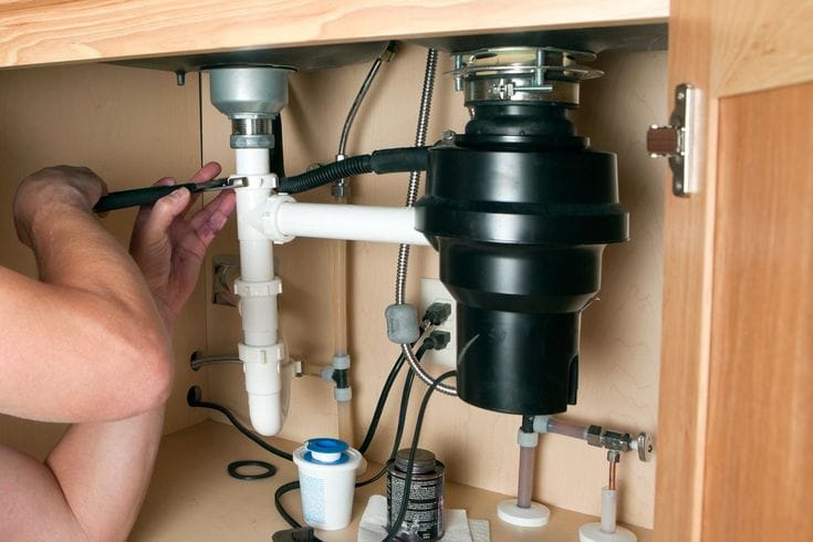 Plumber installing a garbage disposal beneath a kitchen sink in Camas