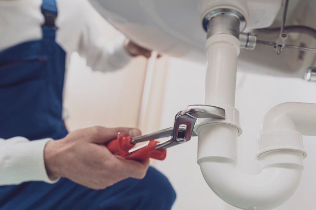 Plumber repairing a white drain pipe beneath a sink in Camas