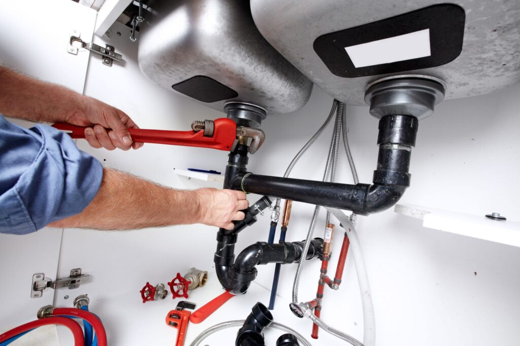 Plumber repairing drain pipes beneath a kitchen sink in Camas